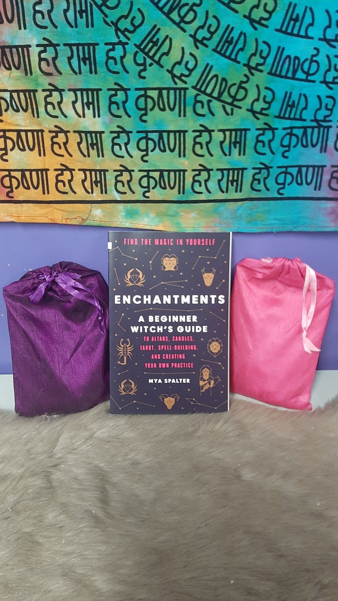 Book titled 'Enchantments' with a colorful patterned fabric and purple bag on a textured surface.